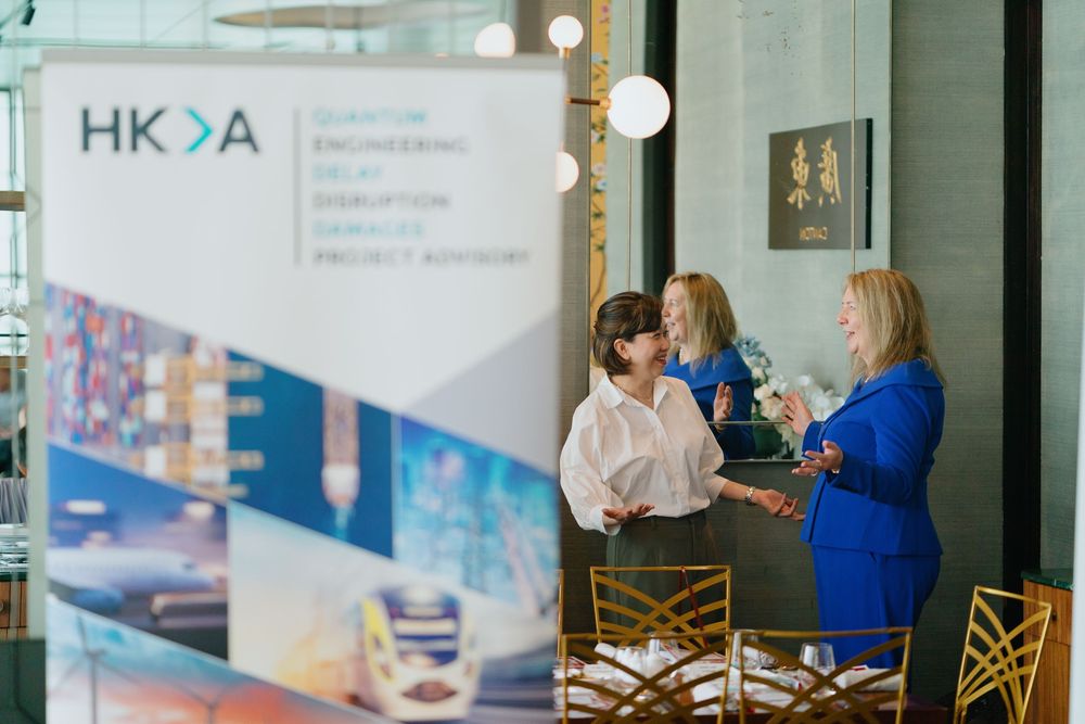 Business professionals having discussions and networking at a corporate event with HKDA banners displayed in the background.