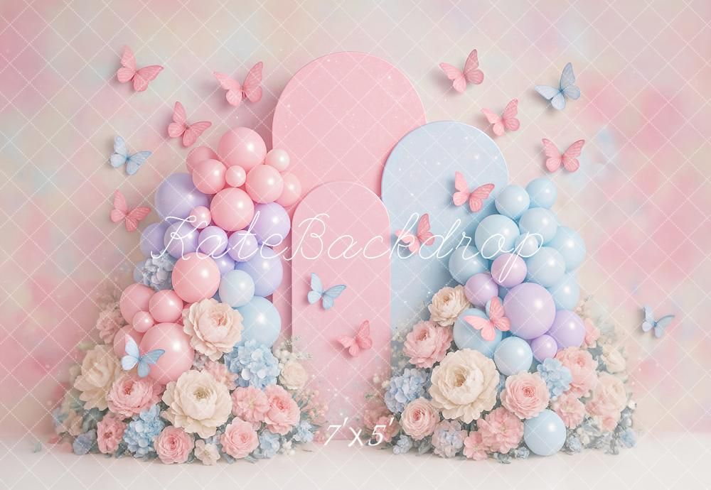 Pastel pink and blue balloon arch with butterflies and floral decorations against a soft dreamy background.