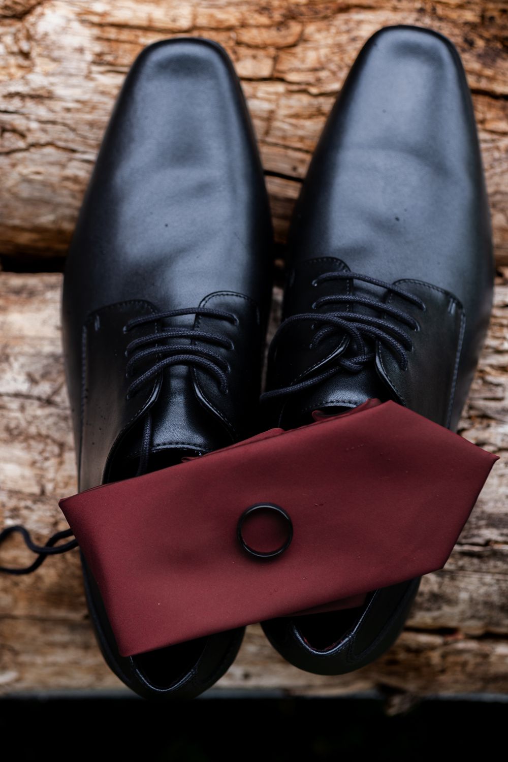 grooms shoes, tie and ring sitting on a pile of wood