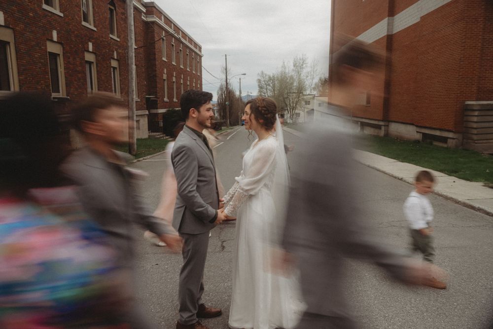 A couple stands together on a rainy city street while people walk past.