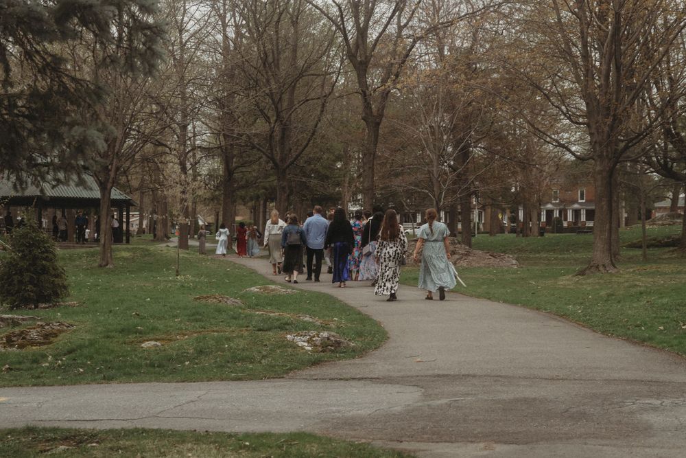 Wedding guests walk along a winding park path on an overcast day.