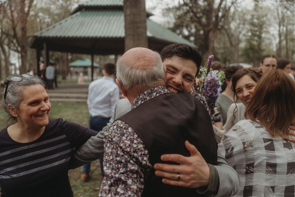 Emotional embrace at an outdoor wedding reception with guests smiling in the background.