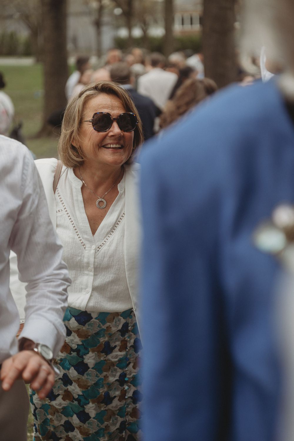 Wedding guest enjoying outdoor celebration in white blouse and patterned skirt.