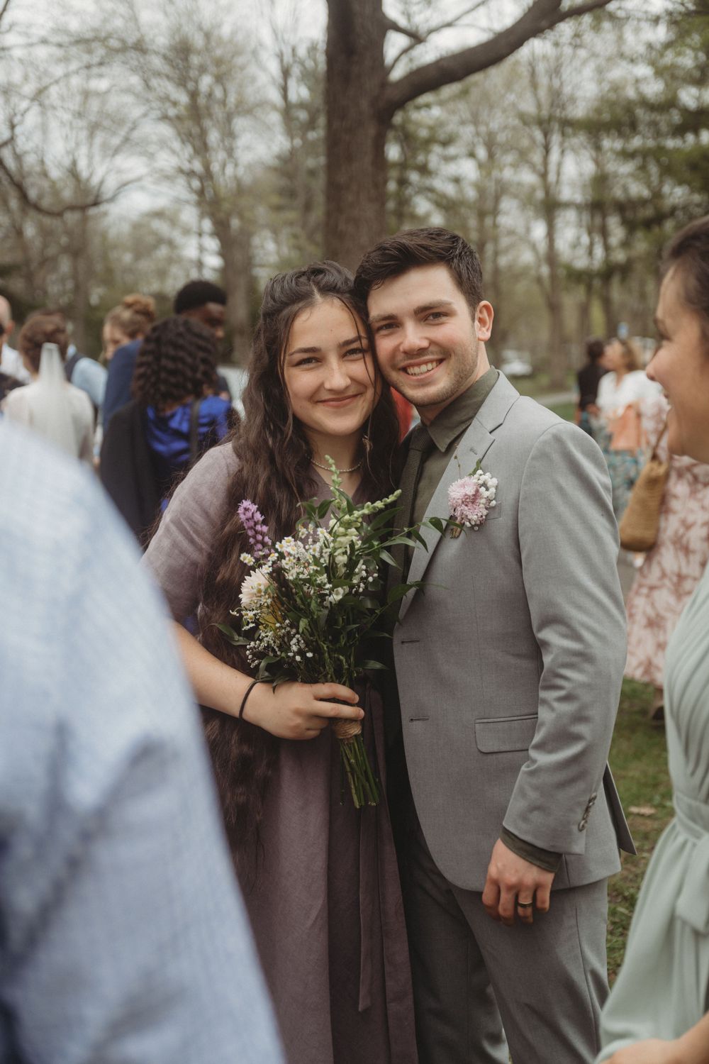 Couple posing with floral bouquet at outdoor wedding celebration.