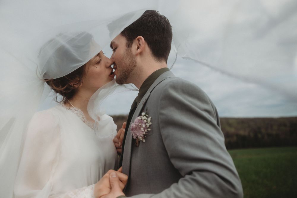 A romantic wedding moment captured outdoors with a grey suit and white dress against nature.
