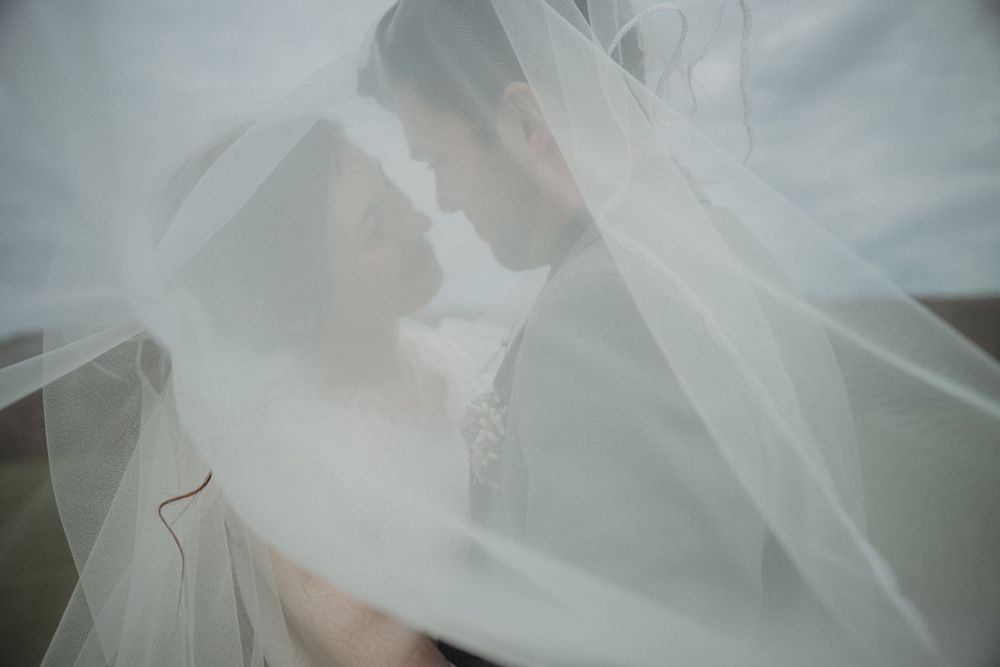 An artistic wedding photo through flowing white veil fabric creating a dreamy effect.
