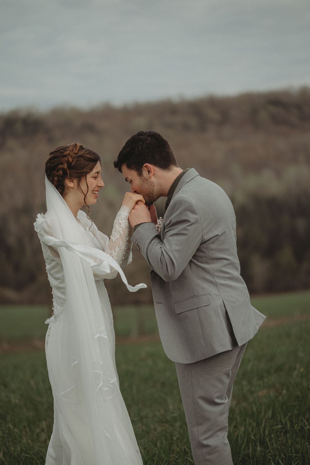 A sweet wedding moment captured in a field with grey suit and lace dress details.