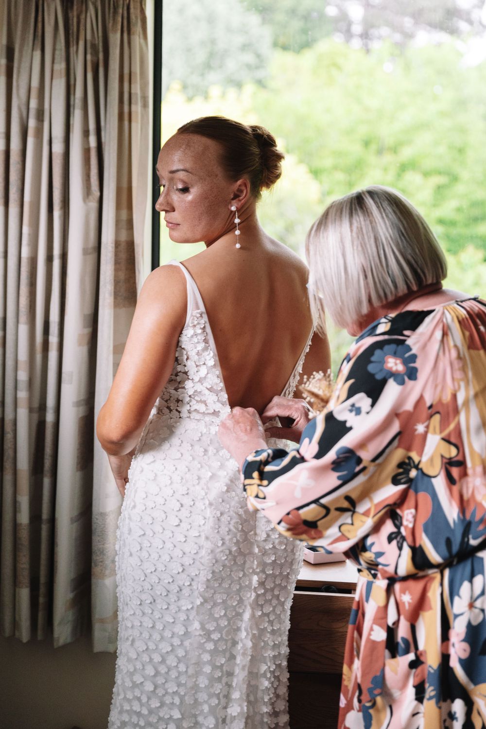 A detailed back view of a bride's lace dress being adjusted for the ceremony.