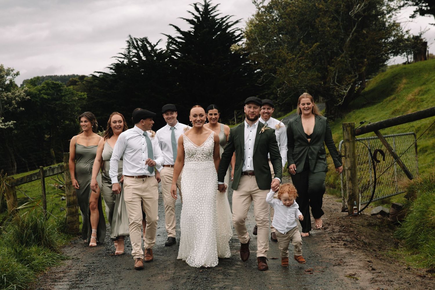 Wedding party walking together on a hillside path during overcast weather.