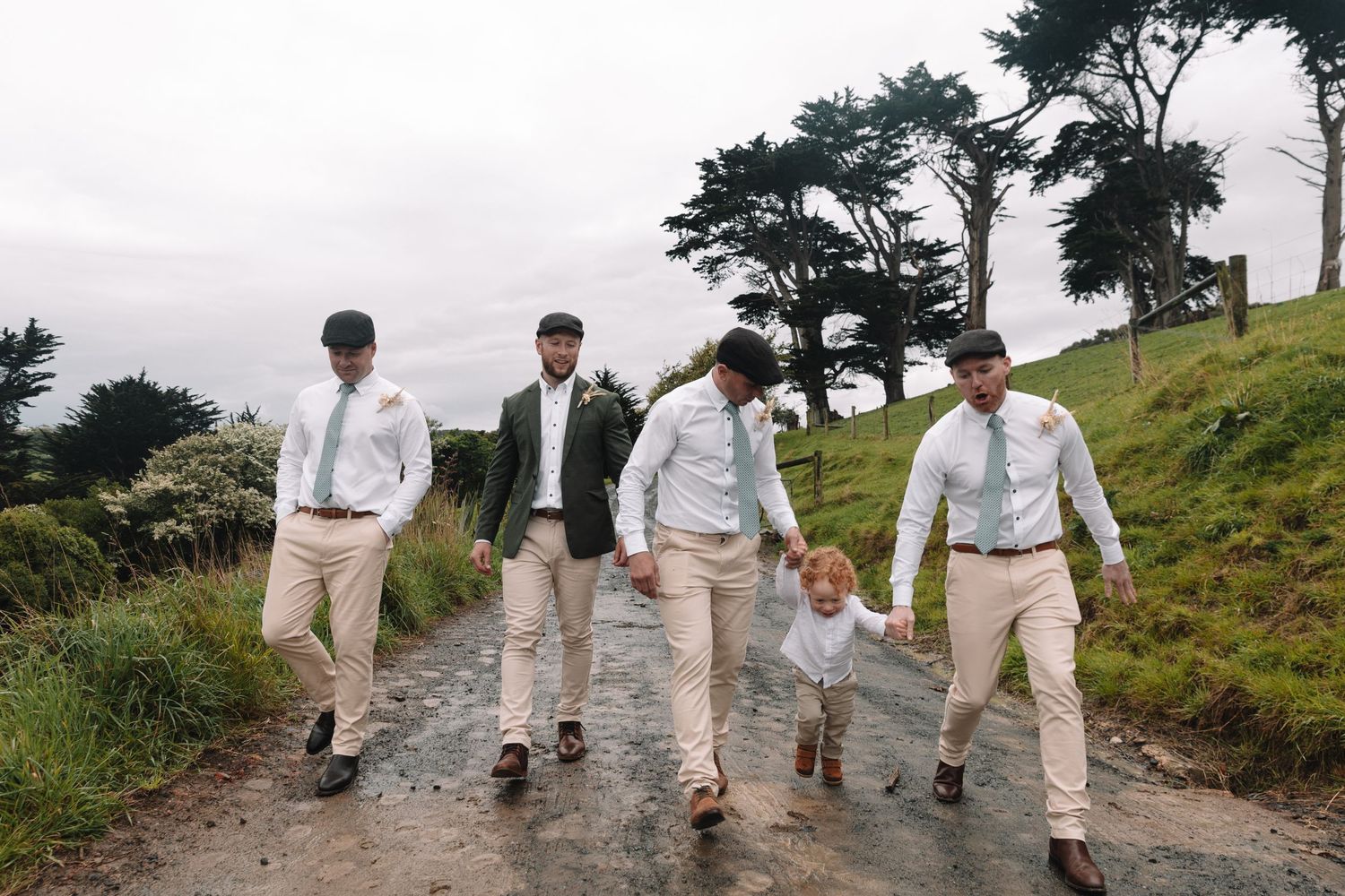 Groomsmen in light colored attire walking down a rustic mountain path.