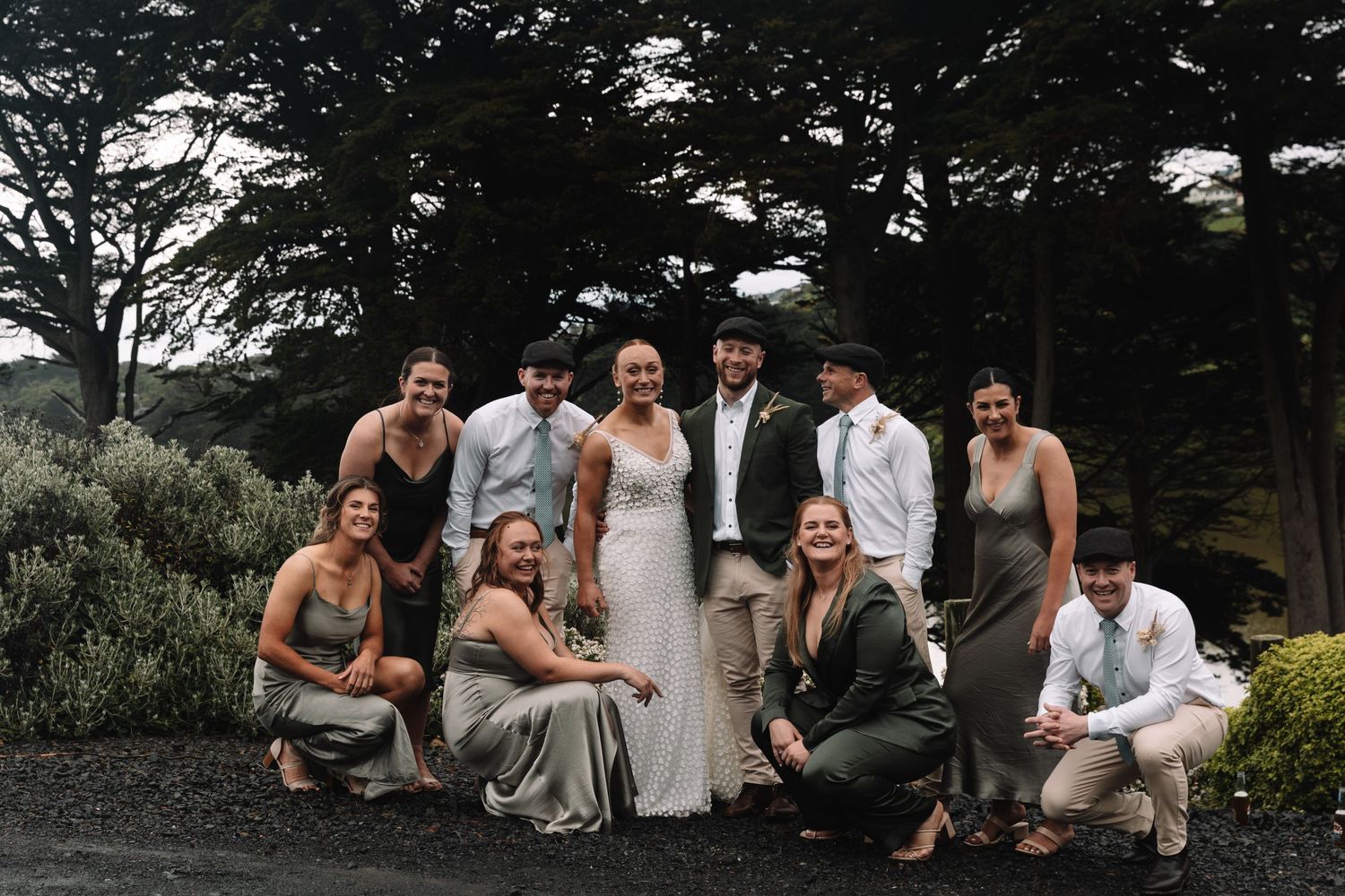 Wedding party poses together in a casual group shot with cypress trees in background.