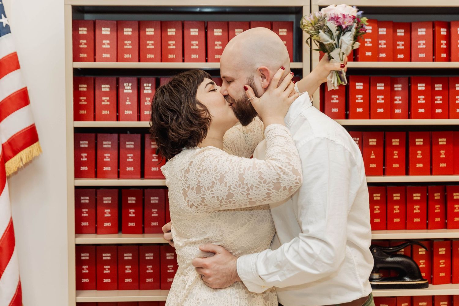 A couple shares their first kiss as newlyweds in front of law library shelves.