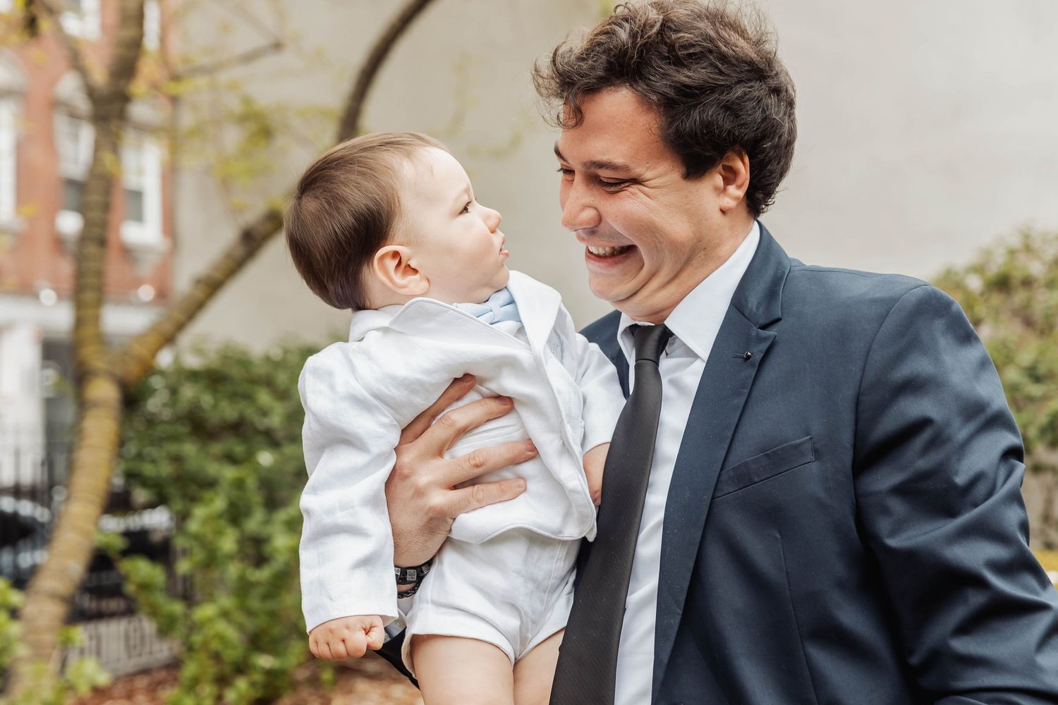Sweet candid moment between parent and child in formal attire outdoors.