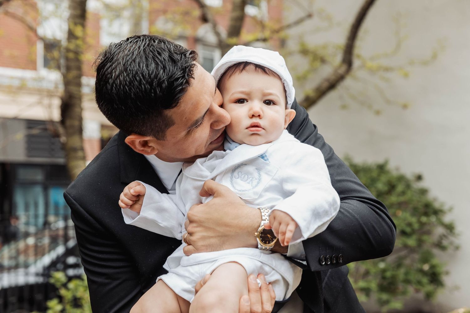 A tender outdoor moment with a baby dressed in white baptismal attire.