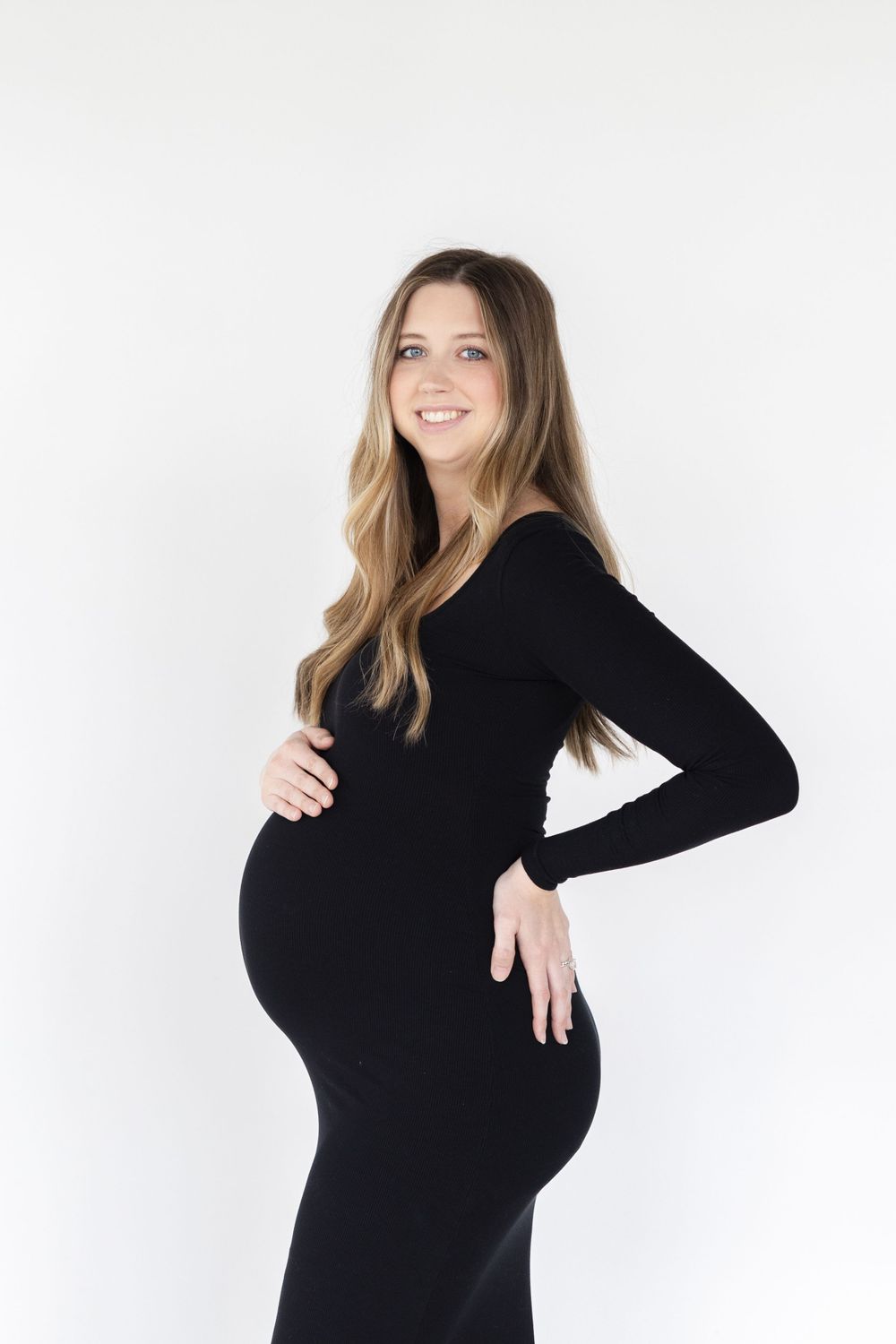 Expectant mother in black dress poses against white background.