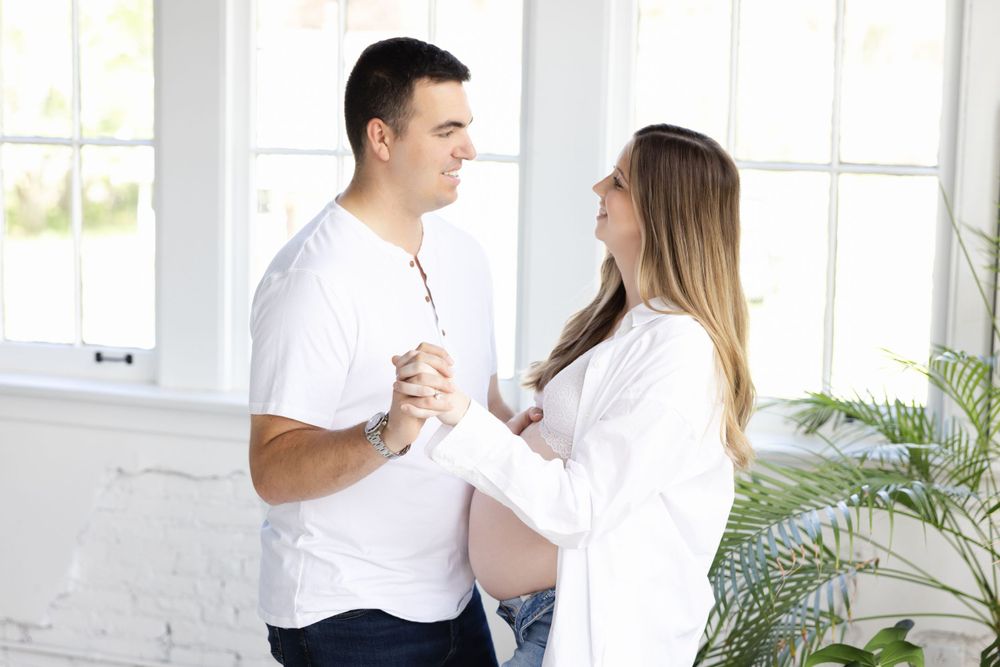 Couple holds hands tenderly in bright white studio setting.