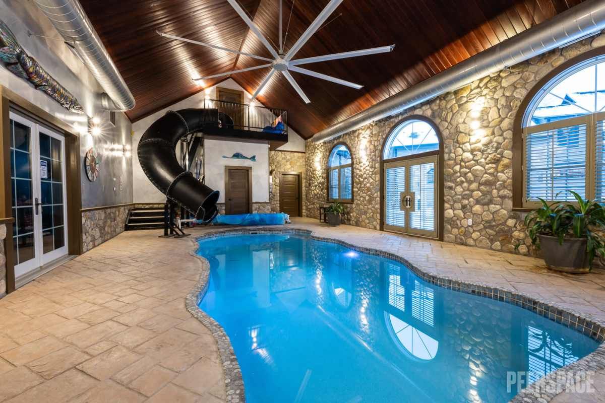 Luxury indoor swimming pool with stone walls, arched windows and wooden beam ceiling.
