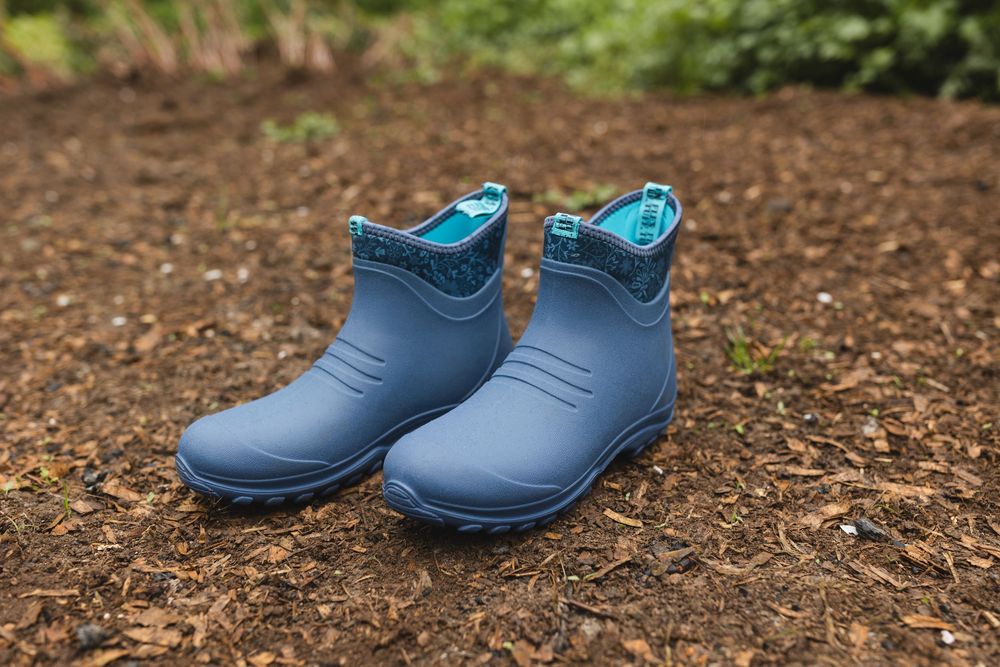 A pair of blue rubber ankle rain boots sitting on brown soil or mulch ground outdoors.