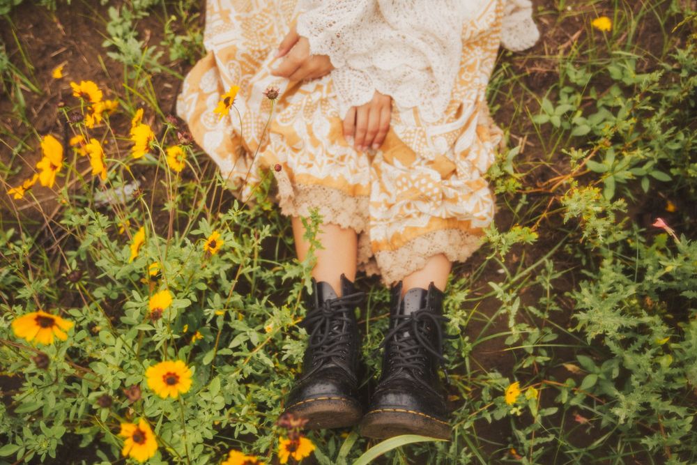 Black leather boots stand amid vibrant yellow wildflowers and green foliage in a meadow.