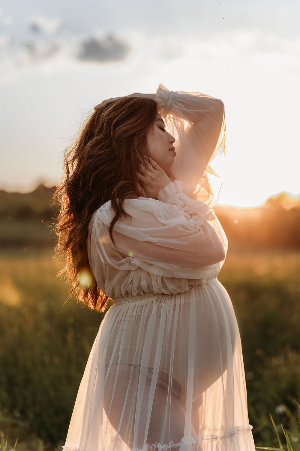 Ethereal maternity portrait in flowing white dress during golden hour sunset.