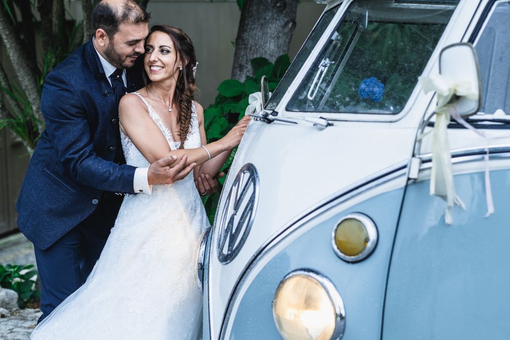 Wedding couple poses by classic light blue Volkswagen van with white ribbons.