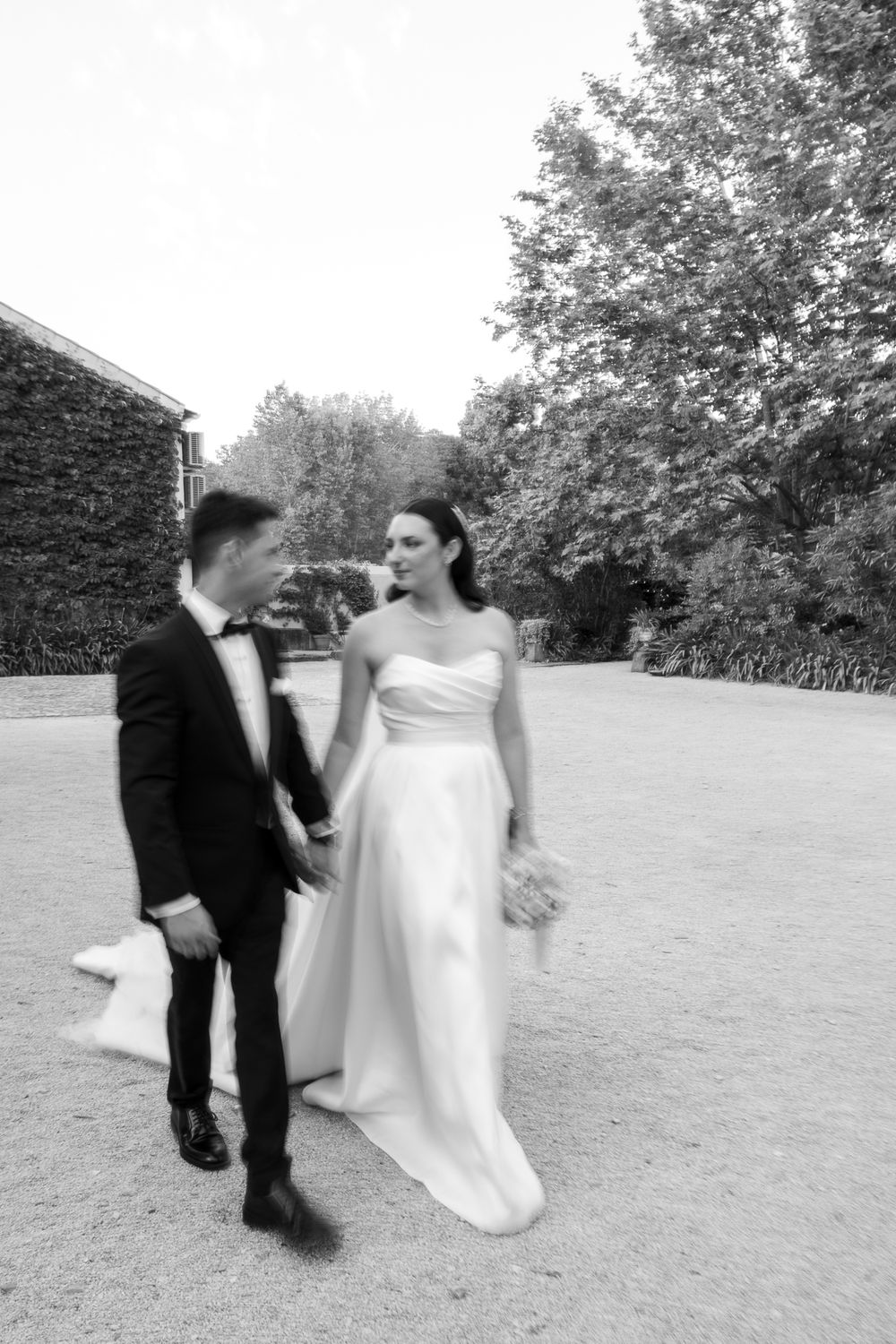 Dancing newlyweds in formal attire twirling on outdoor garden grounds.