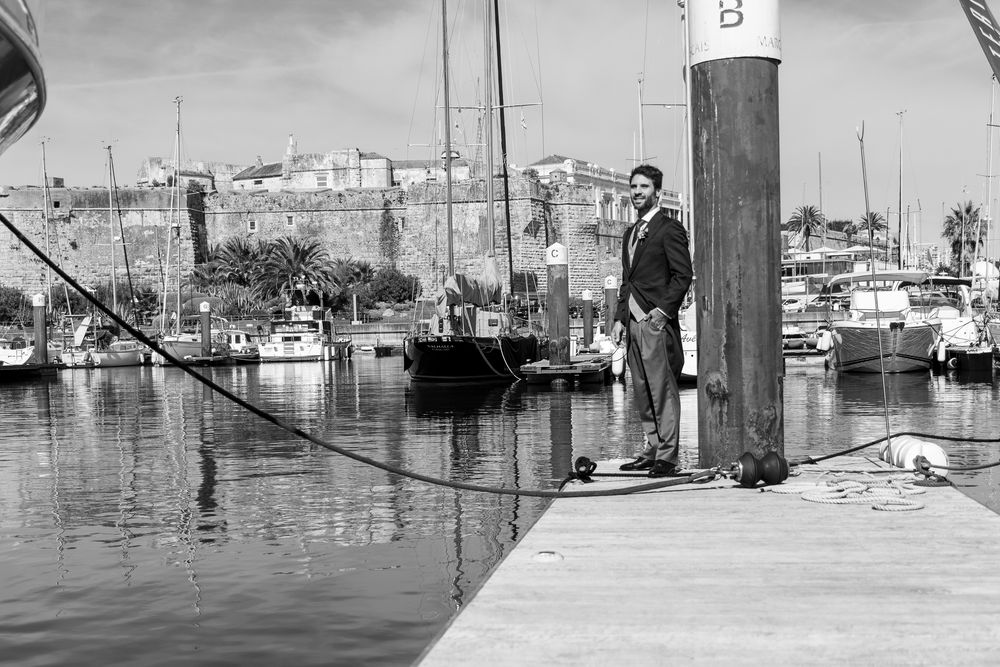 Black and white photo of a person standing on a dock at a marina with boats in background.