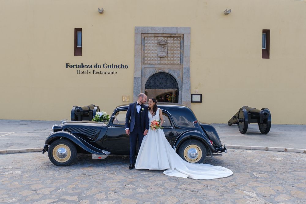 A wedding photoshoot with a classic black vintage car against a beige building facade.