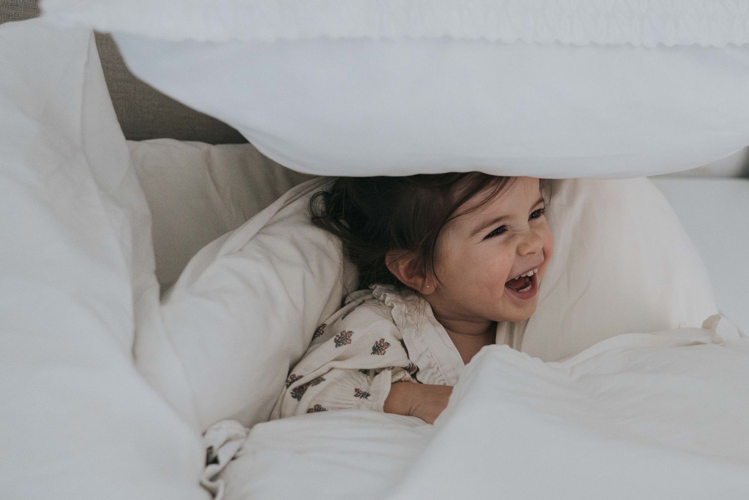 niña riendo entre sábanas blancas durante una sesión de fotos familiar en casa en Madrid
