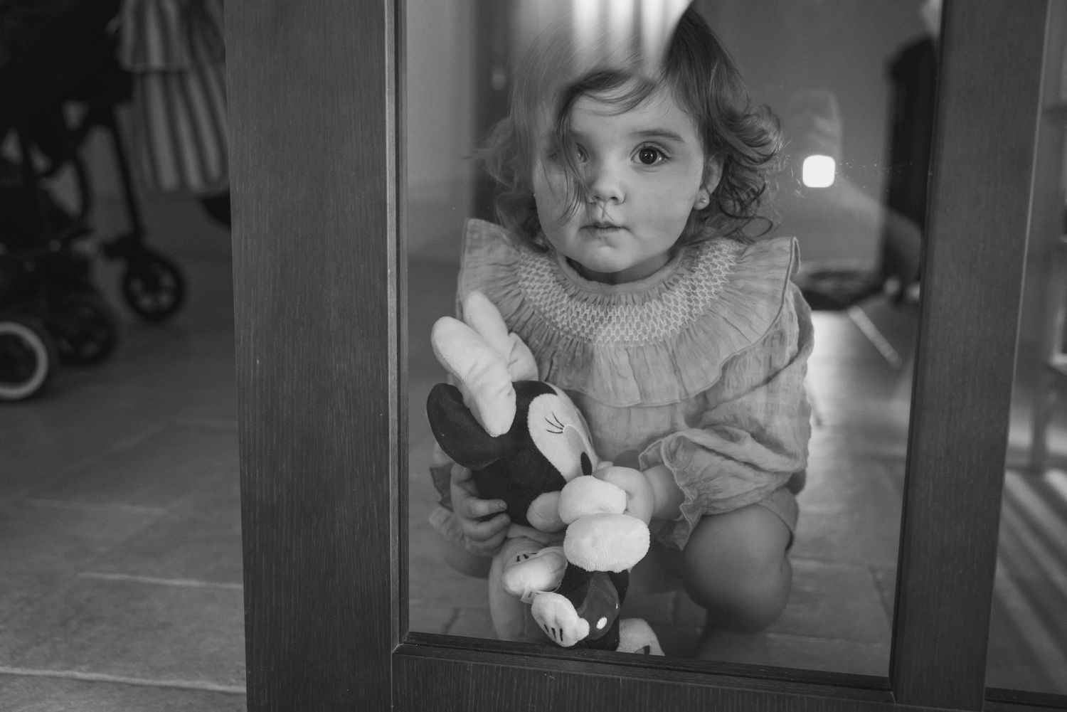 niña con muñeco mirando a través de una puerta de cristal durante una sesión de fotos familiar natural en casa en Madrid