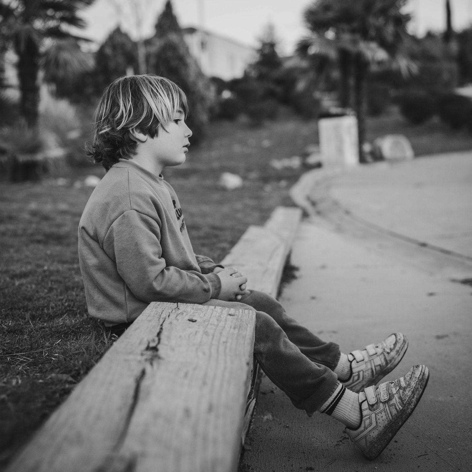 chico sentado, pensativo, enfadado en el parque Infantil El Oro en Torrelodones. Fotografia de calle en blanco y negro