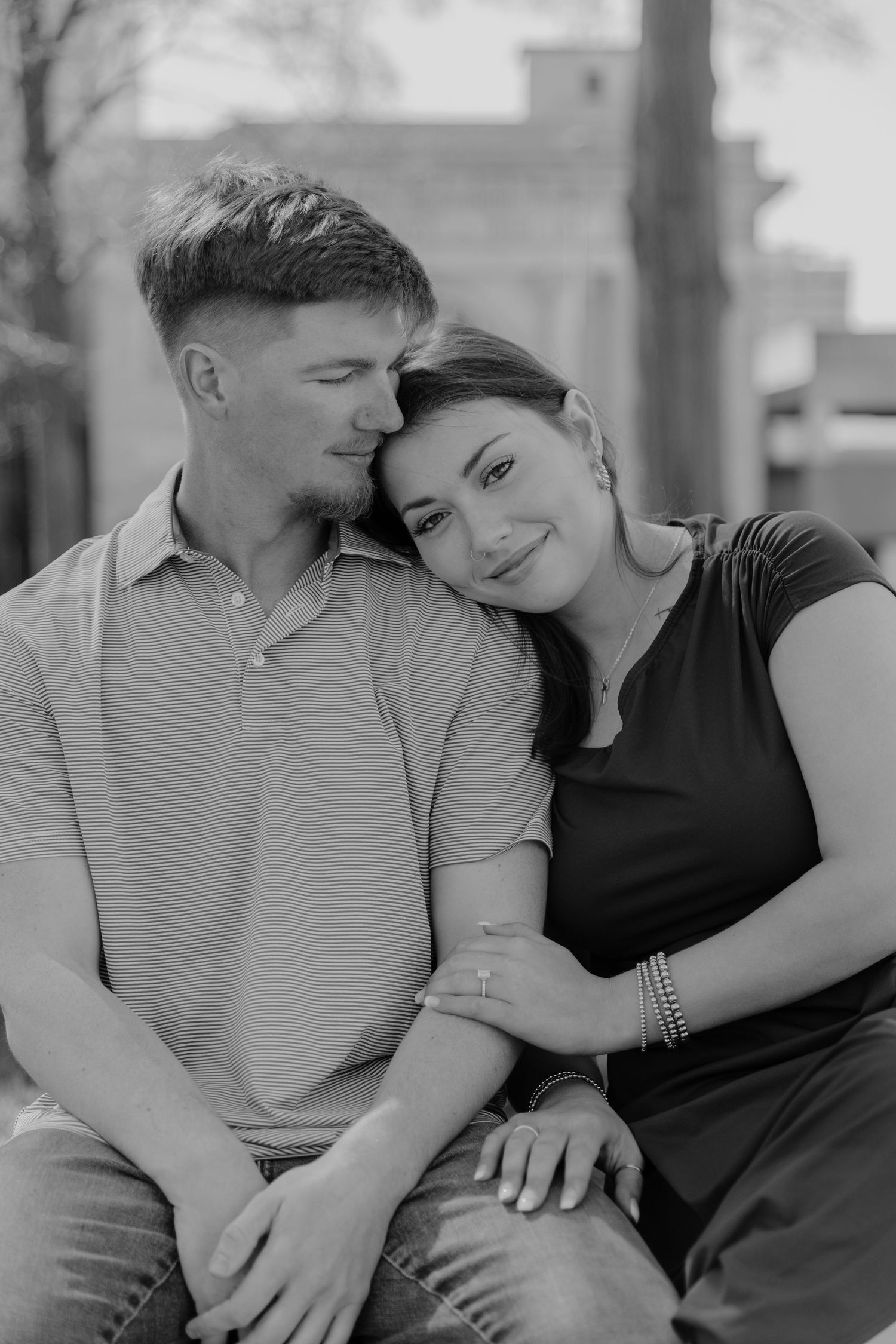 A romantic black and white portrait of a couple embracing and smiling together while sitting outdoors.