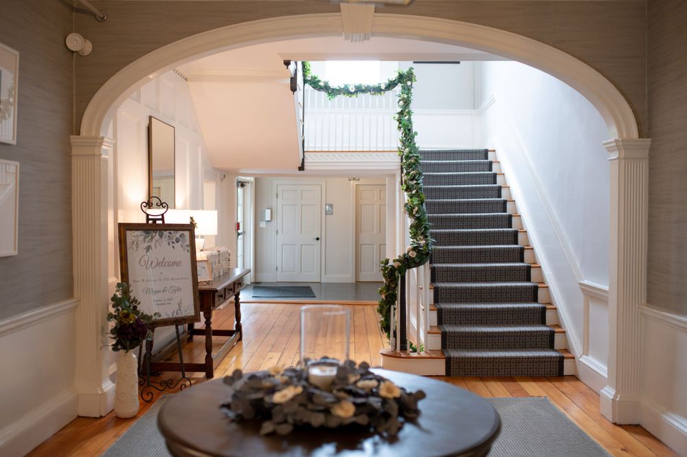 An elegant entryway with arched doorway, grey staircase, and festive holiday greenery.