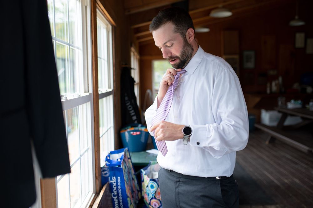 A person adjusts their tie while getting ready in a rustic wooden room with windows.