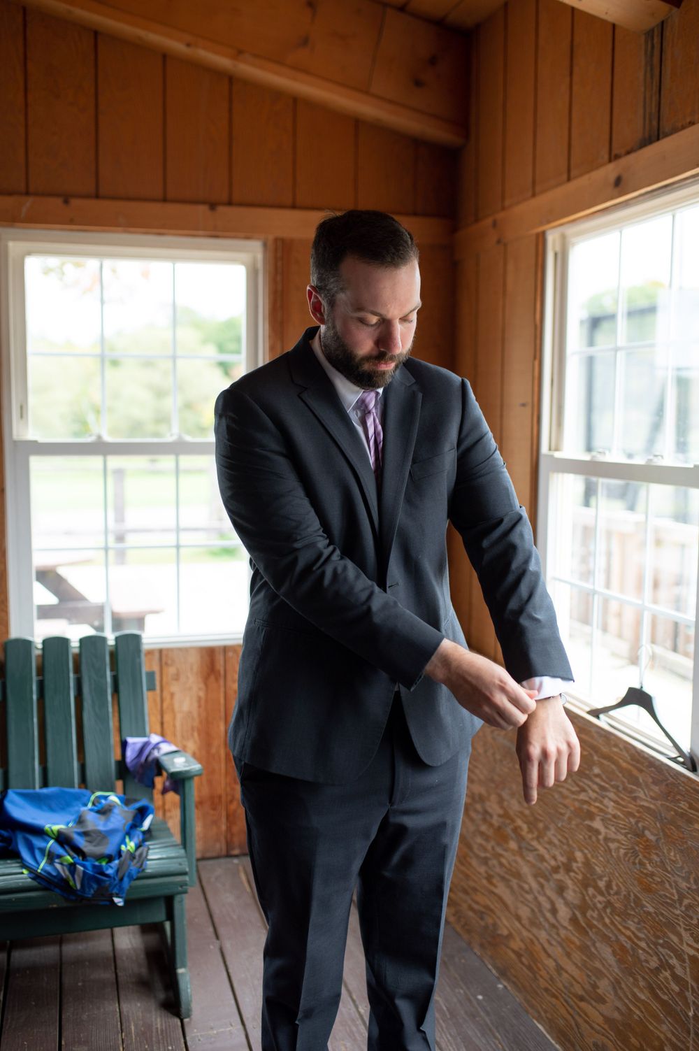 A person in a dark suit adjusts their cuffs in a sunlit wooden room.