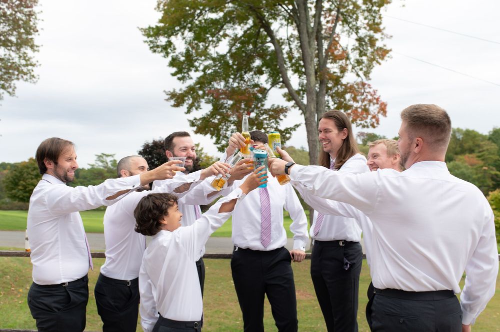 Wedding party raises their drinks in a celebratory toast on a wooden deck outdoors.