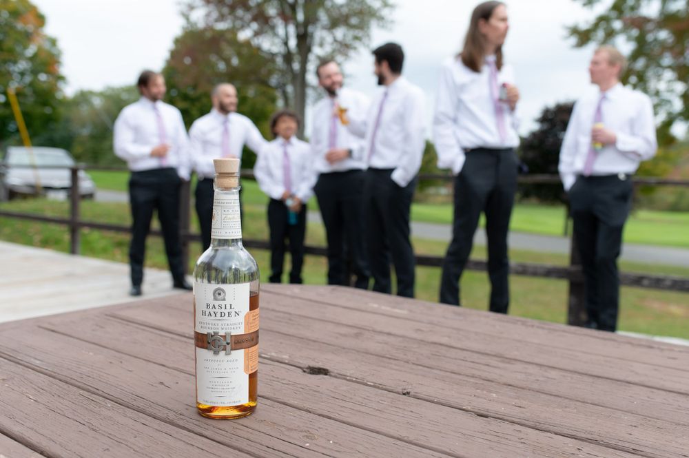 A bottle of liquor sits on wooden deck with people gathered in background.