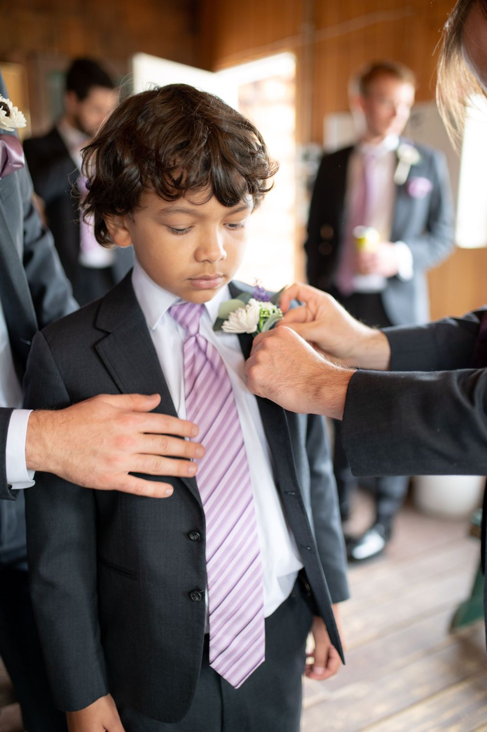 A young attendant in a formal suit and pink tie has a boutonniere pinned to his lapel.