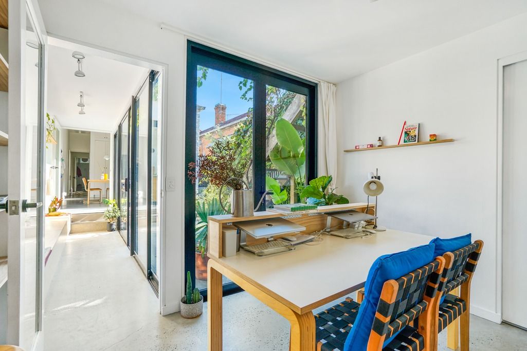 Light-filled dining nook with wooden table, blue chairs, and floating shelves.