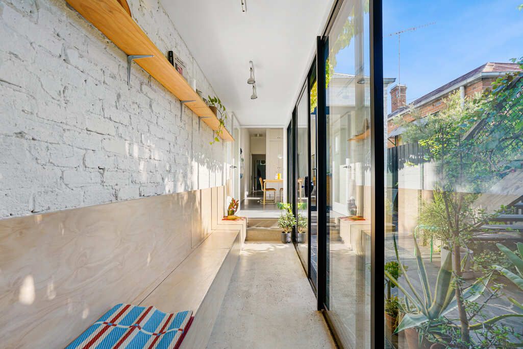 Modern hallway with white brick walls, wooden shelf, and floor-to-ceiling windows letting in natural light.