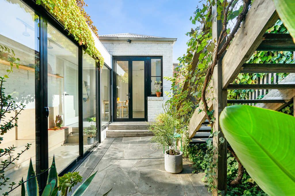 Modern glass walkway with white walls and tropical plants creating a garden atmosphere.