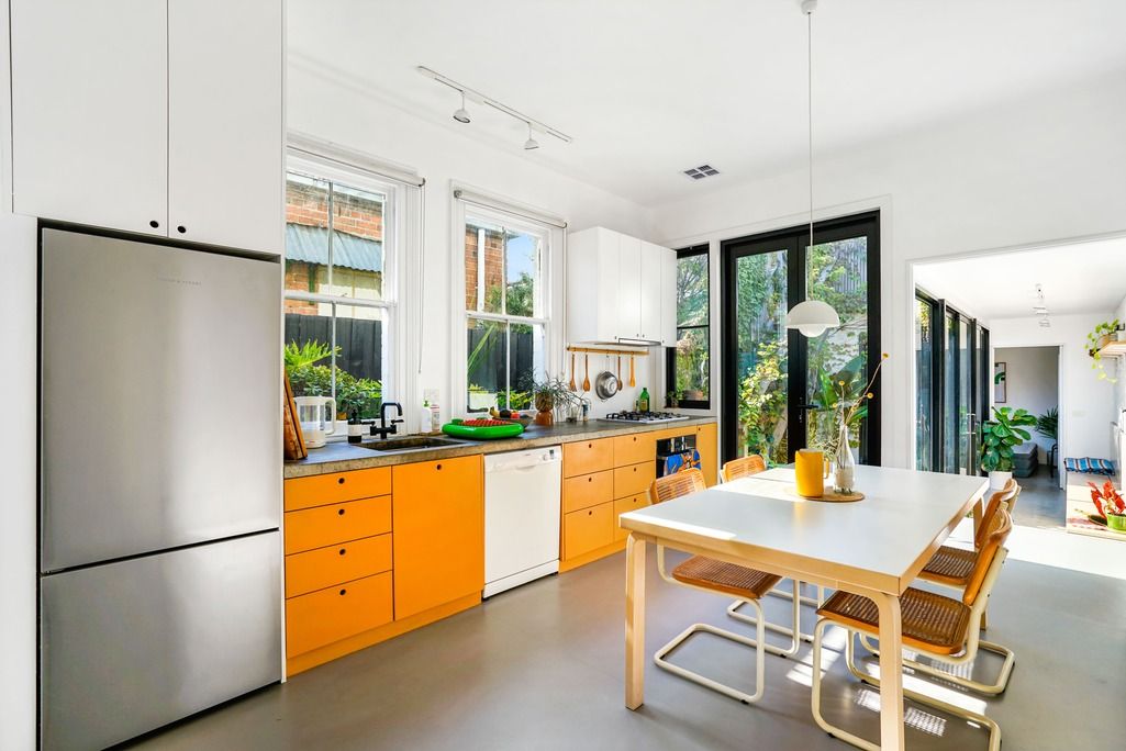 Bright modern kitchen with orange cabinets, stainless appliances, and wooden dining table.