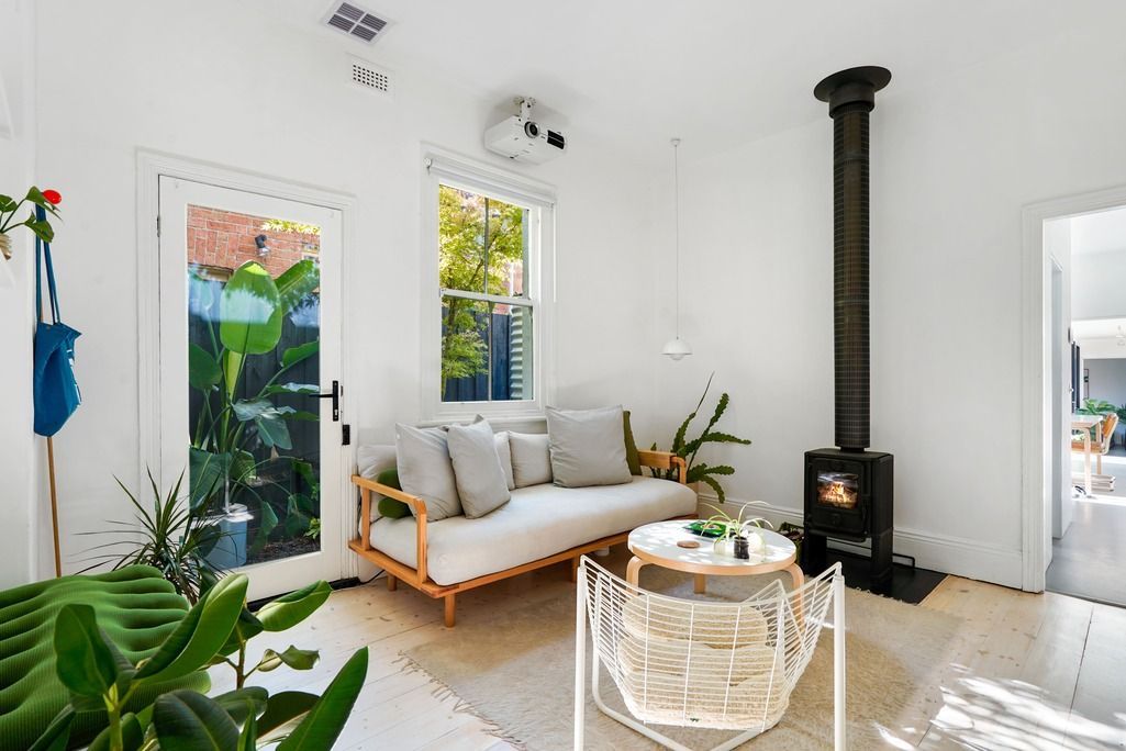 Cozy living space with white sofa, black wood stove, and large windows bringing in natural light.