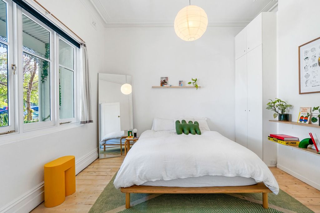 Minimalist white bedroom with round pendant light, wooden floors, and bright windows.