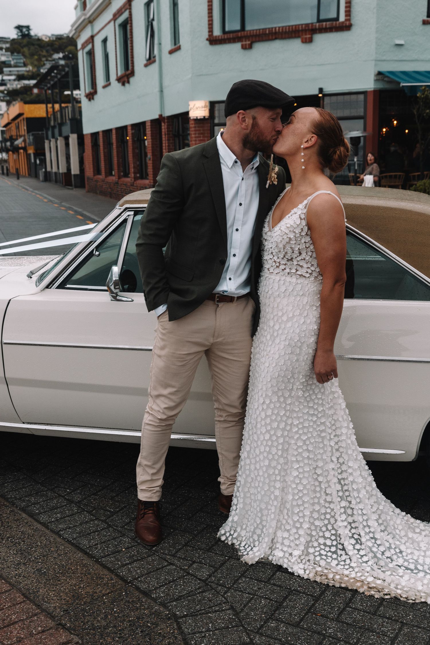 Couple shares romantic moment beside vintage car on urban street.