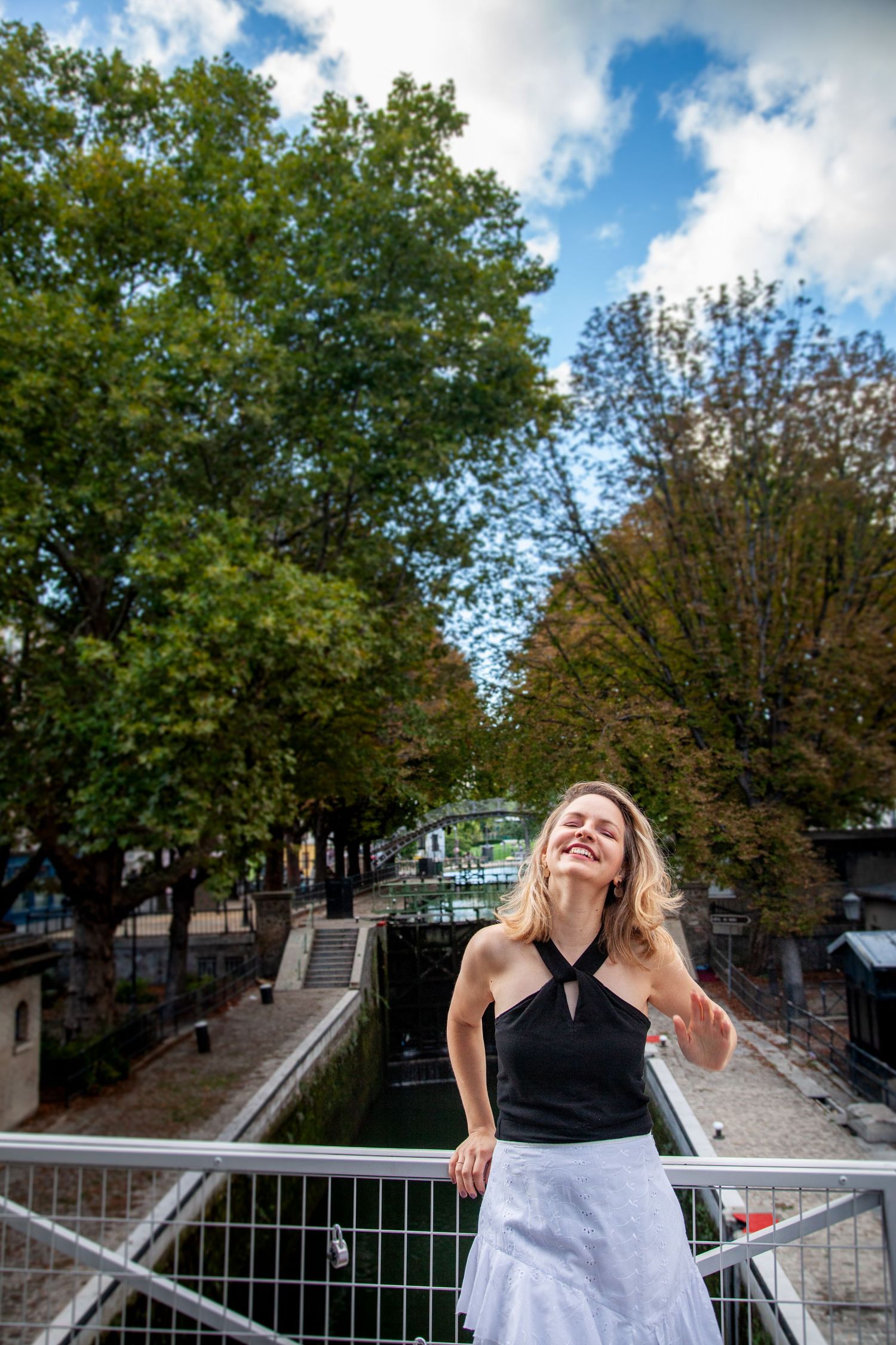 Sunny outdoor scene with trees and blue sky along a canal railing.