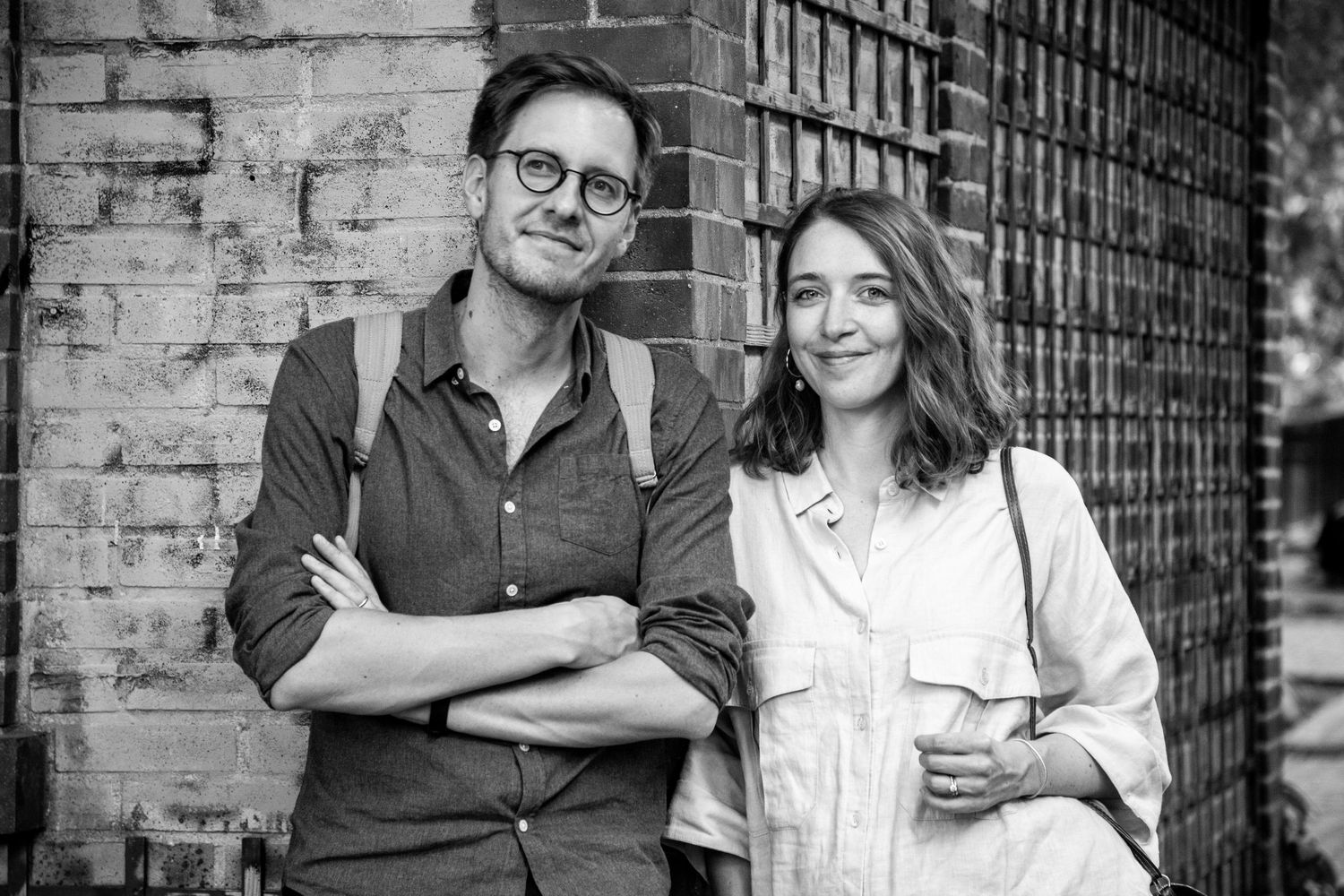 Couple poses against brick wall in casual attire for black and white portrait.