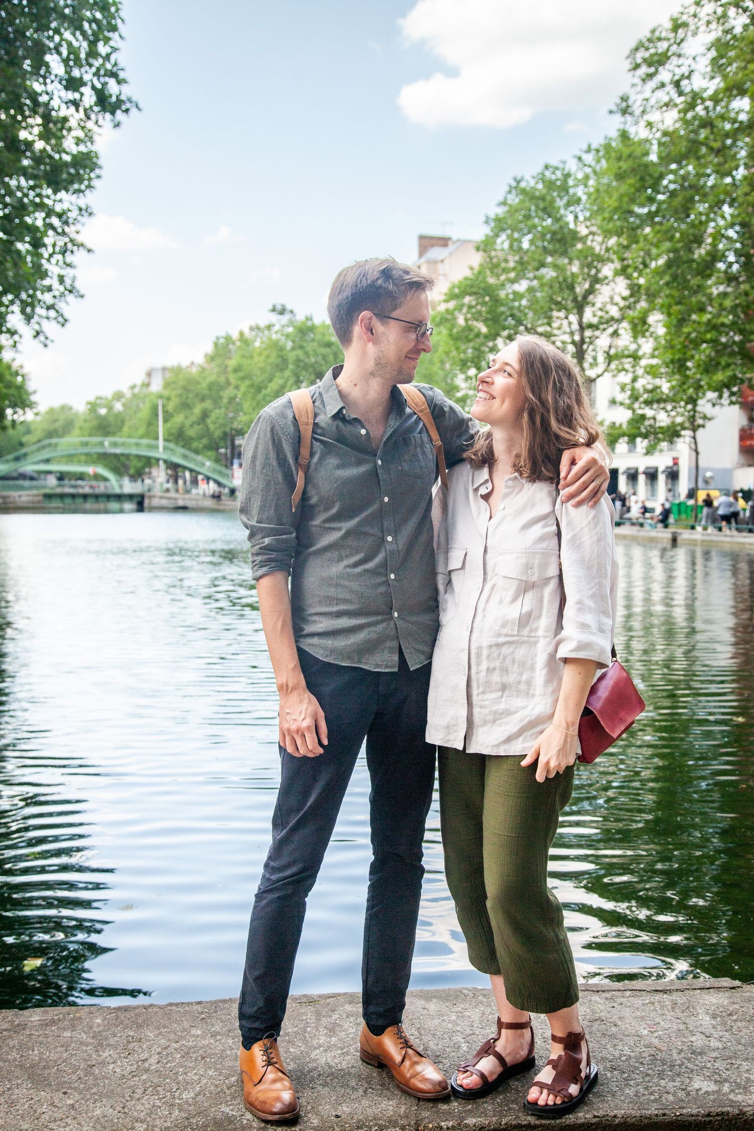 Couple shares romantic moment along canal with bridge and trees in background.