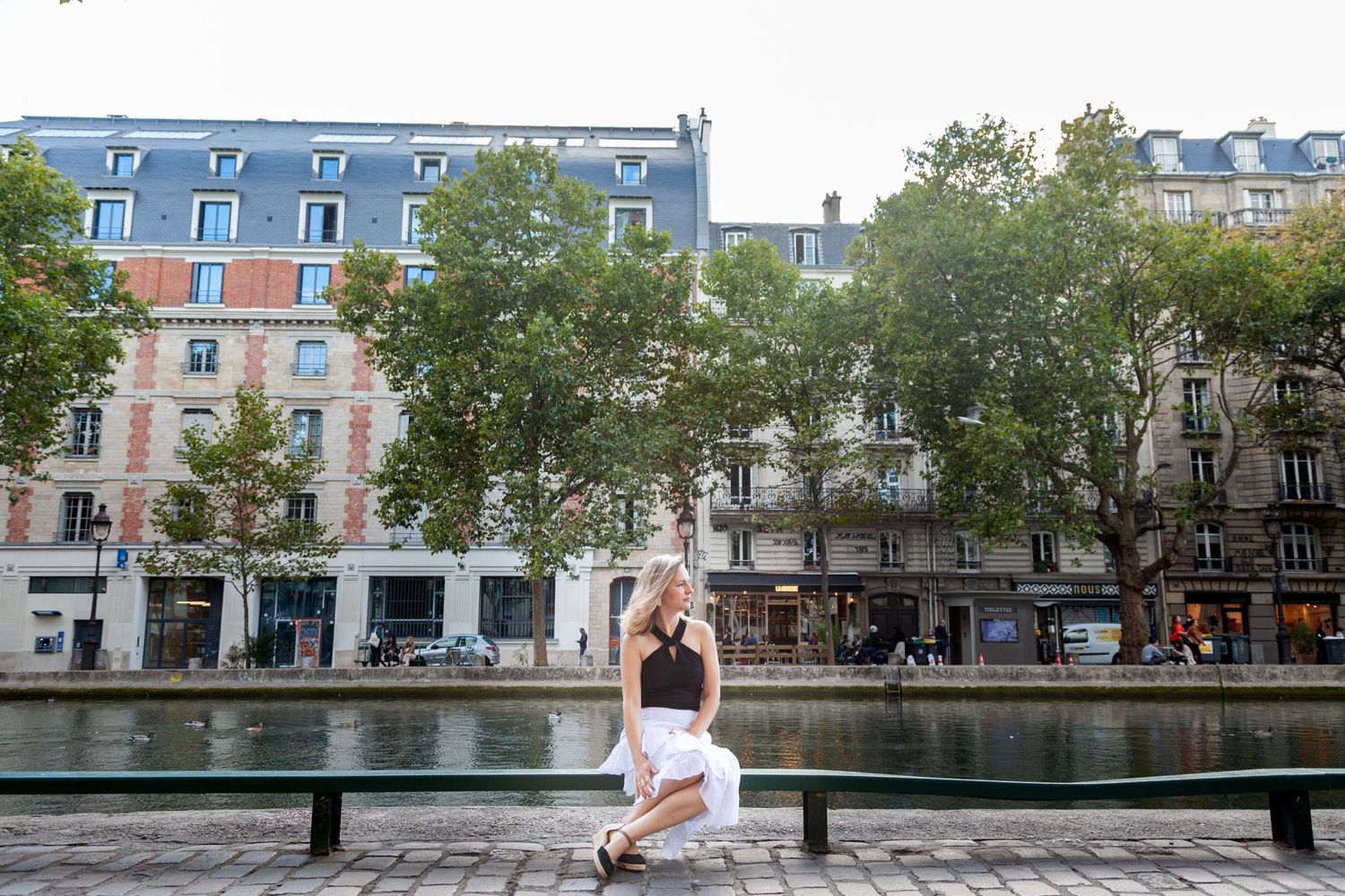 Canal-side view of historic Parisian buildings with trees lining the waterway.