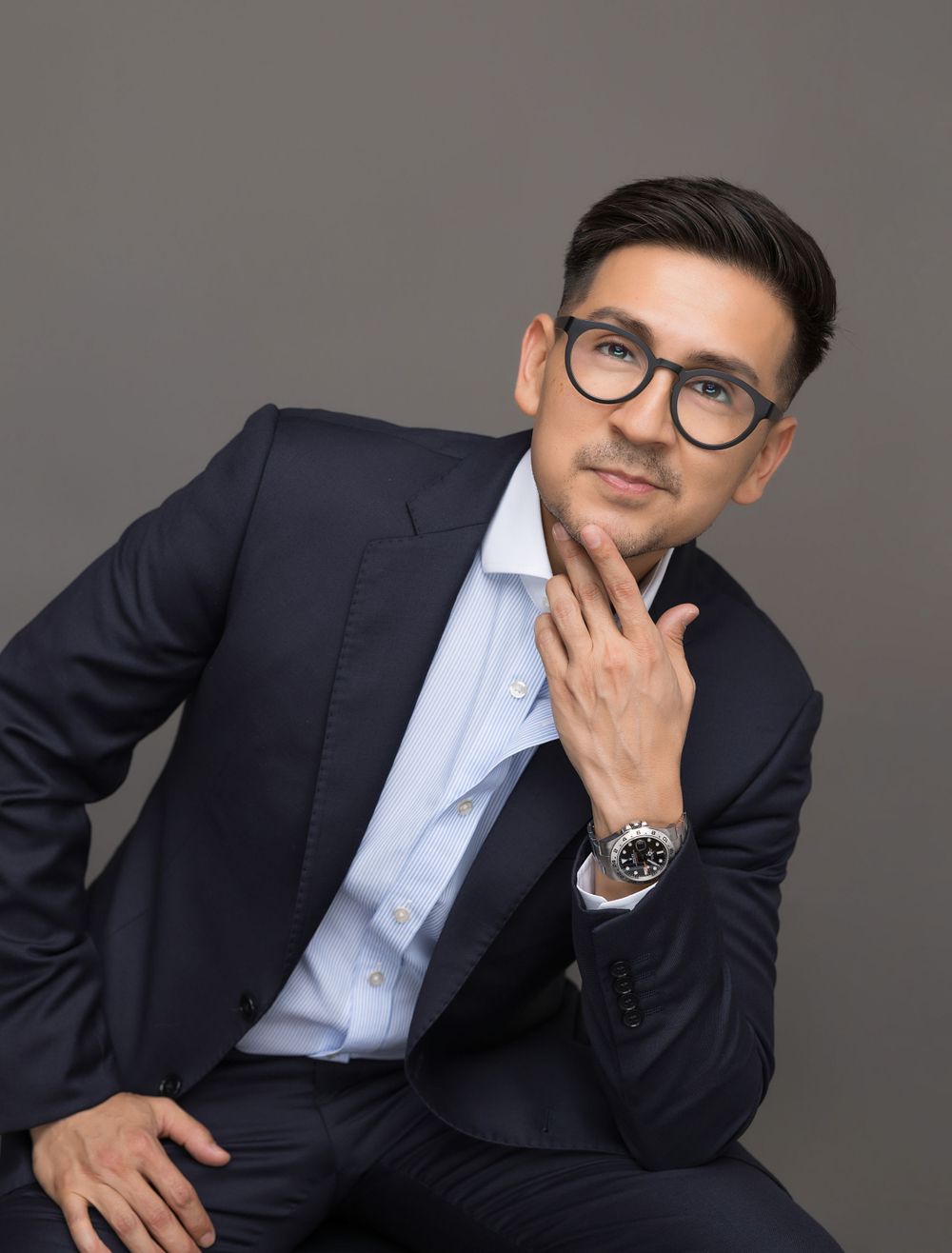 Professional headshot of man in navy suit and glasses with thoughtful expression.